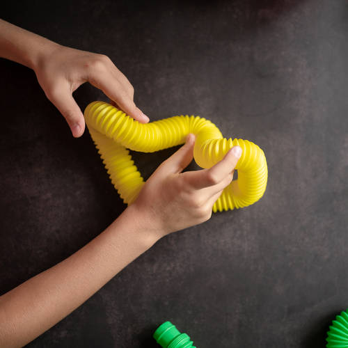 anti stress sensory pop tube toys in a children’s hands. a little happy kids plays with a poptube toy on a black table. toddlers holding and playing pop tubes multicolor bright color, trend 2021 year