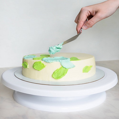 hands with a spatula decorate the cake with green and blue cream